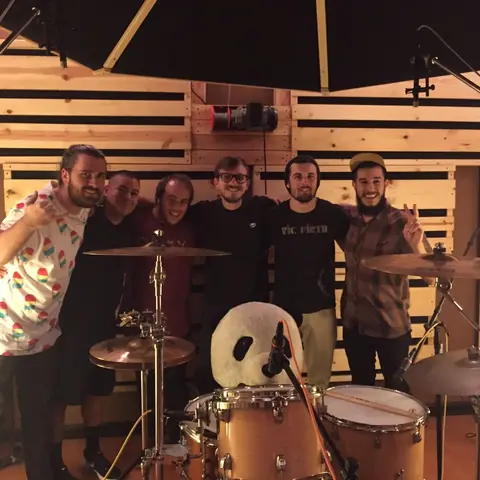 A band and friends behind the drum kit with the panda plush, 2015