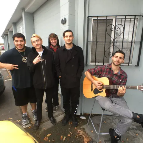 A band hanging out outside the studio, one playing acoustic guitar, 2016