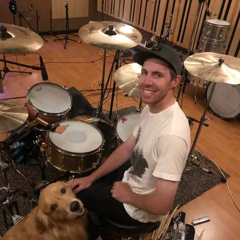 A drummer at the kit with the studio dog leaning on him, 2020