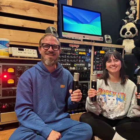 Sam Pura and Theresa Brown holding up microphones in the West control room, 2025